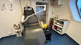 Lääkärin työtilassa on lääkärintuoli ja muun muassa hyllyjä.