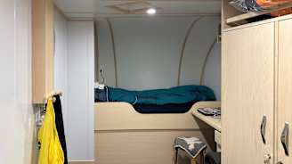 Hytissä on vuode ja henkilökohtaisia tavaroita kuten laturi ja kuulokkeet.