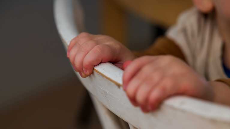 Barnhänder håller i en stolsrygg.