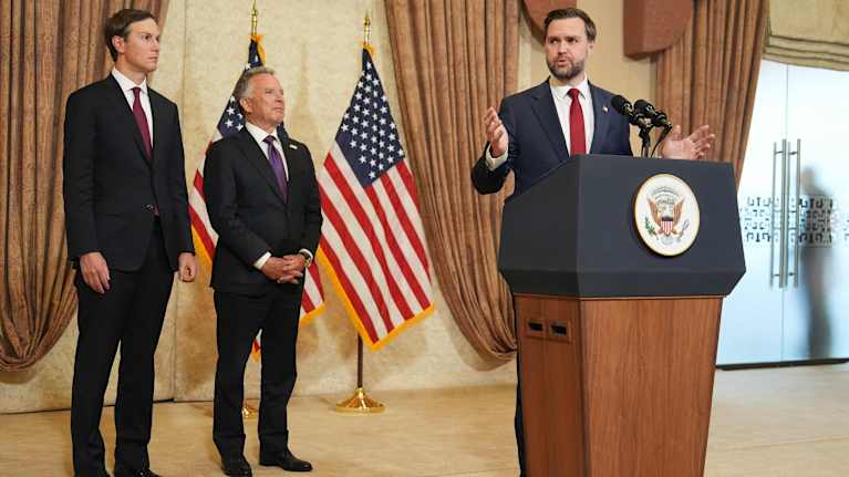 JD Vance puhuu puhujankorokkeella. Witkoff ja Kushner seisovat vierellä.
