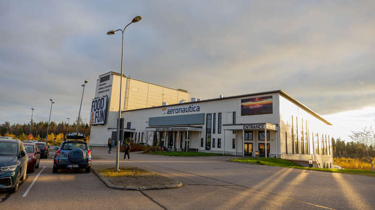 Flera bilar står parkerade utanför en byggnad med skyltarna "FOOD & FUN", "aeronautica" och "ENTRANCE".