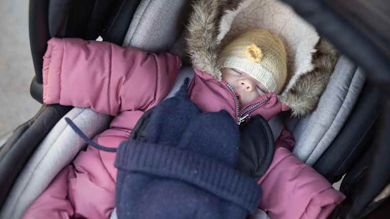 Newborn baby dressed in warm winter outerwear, sleeping in a pram.