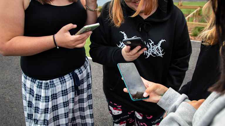 High school girls in a circle with phones in their hands.