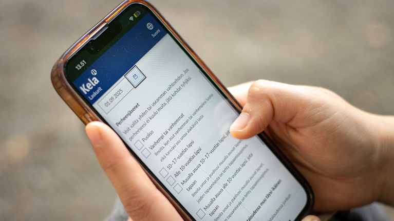 Close-up of hands holding a phone. The Kela social assistance calculator is open on the phone.