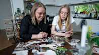 Äiti Reija Jyrkinen (vas) ja 16-vuotias tytär Kaisa Jyrkinen tutkimassa Reijan vanhoja Interrail-häämatkan valokuvia perheen keittiönpöydän ääressä.
