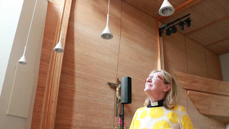 En kvinna med glasögon och prästkrage som tittar uppåt inne i en kyrka.