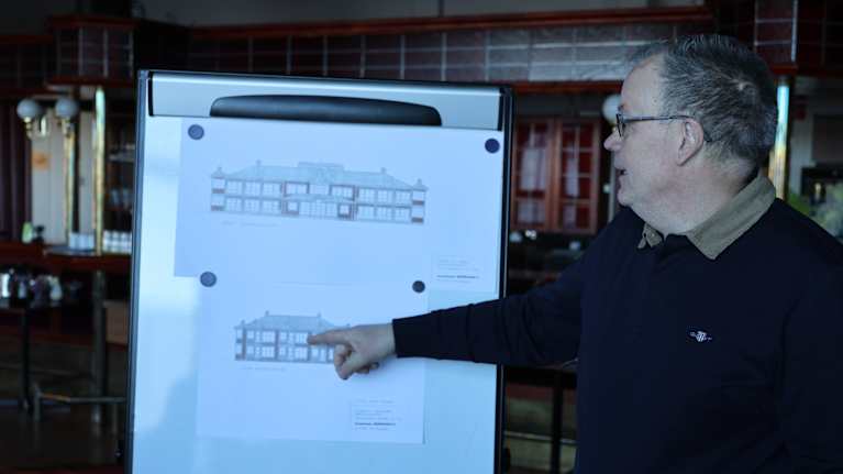 En man pekar på ritningar av en stor byggnad.