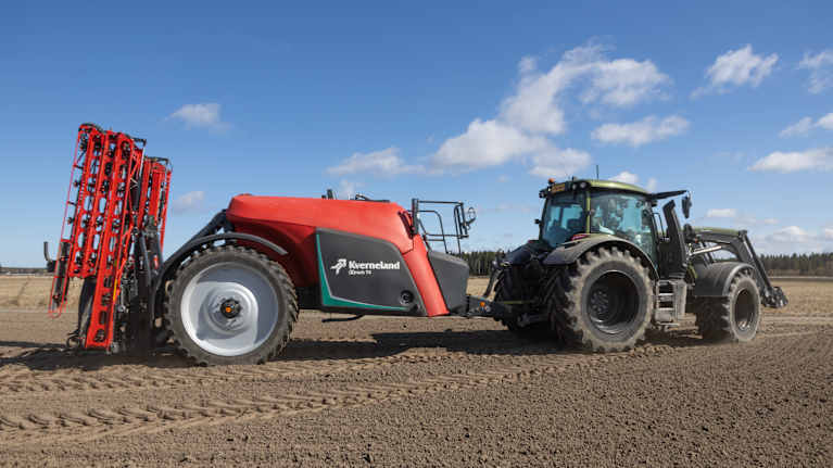 En traktor med jordbruksmaskin körs över en åker under en klar himmel.