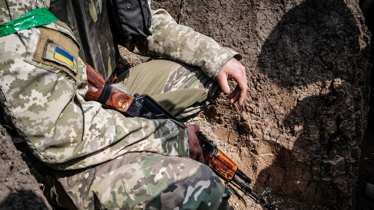 Ukrainalainen sotilas istuu ase kädessä juoksuhaudassa.