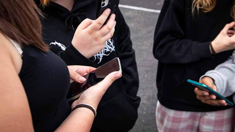 Teens standing next to each other, holding smartphones.