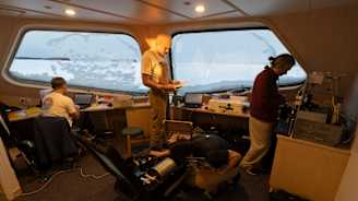 Neljä ihmistä työskentelee laitteiden parissa aluksella.