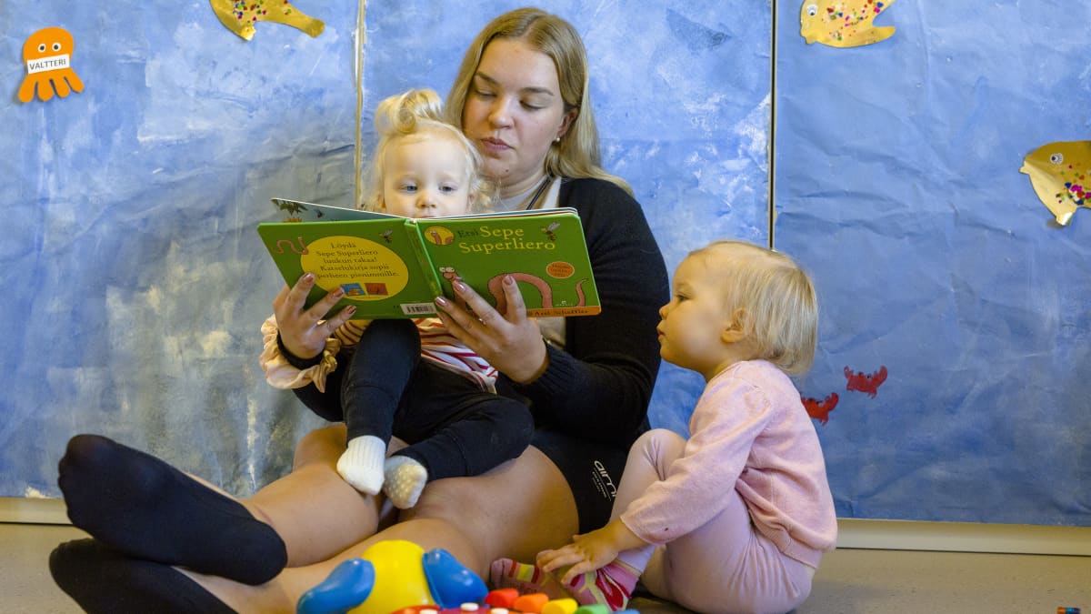 Päiväkodinhoitaja lukemassa kirjaa lapsille.