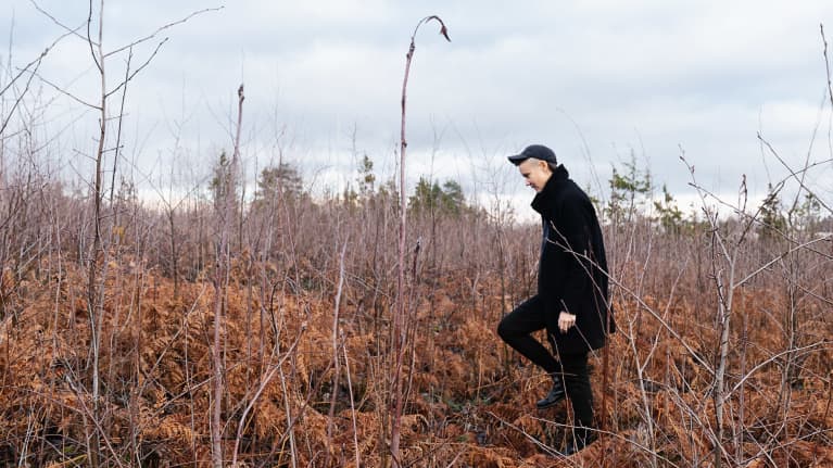 Emilia Kokko kävelee joutomaalla marraskuussa, risukkoa ja kuihtuneita saniaisia.