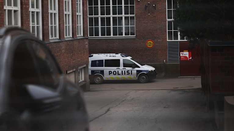 Poliisiauto päivystää rakennuksen sisäpihalla harmaana päivänä.