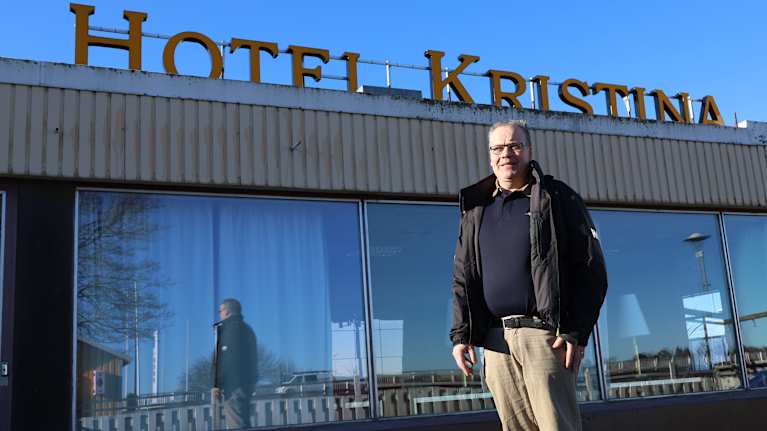 En man står utanför en byggnad. Ovanpå byggnaden står en skylt med texten hotell Kristina.
