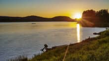 The midnight sun near Tornio in June 2020. The scenery includes a river bay, trees and grass.