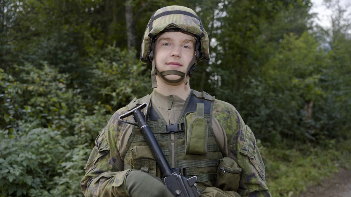 Nuori varusmies sotilasvarusteissa katsoo suoraan kameraan.