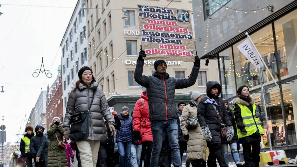 Venäjänkieliset suomalaiset osoittavat mieltään kylttien kanssa kävellen kadulla.