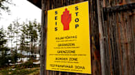 A yellow sign on a weathered wooden wall with a red hand and the words BORDER ZONE in several languages.