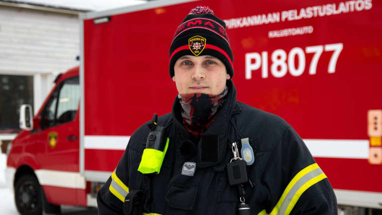 VPK:n vaatteisiin pukeutunut Heikki Isomäki seisomassa Ruoveden paloaseman pihamaalla. Taustalla paloautoja.