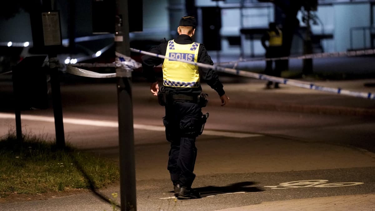 Poliisi kävelee keltaisessa liivissä selin pimeässä illassa paikassa, jossa hänen poliisikollegansa ammuttiin. 