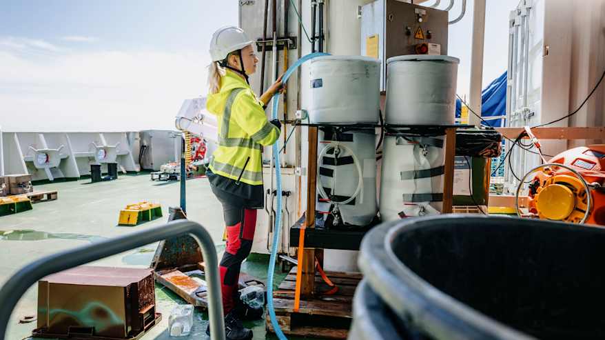 Kuvassa näkyy henkilö, joka työskentelee laivan kannella huomioliivissä ja suojakypärässä.