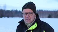 En man mössa och glasögon står i ett vinterlandskap.