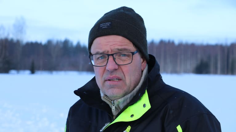 En man mössa och glasögon står i ett vinterlandskap.