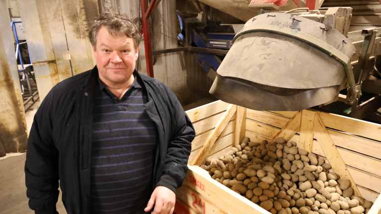 En man står bredvid en halvfull låda med potatis.