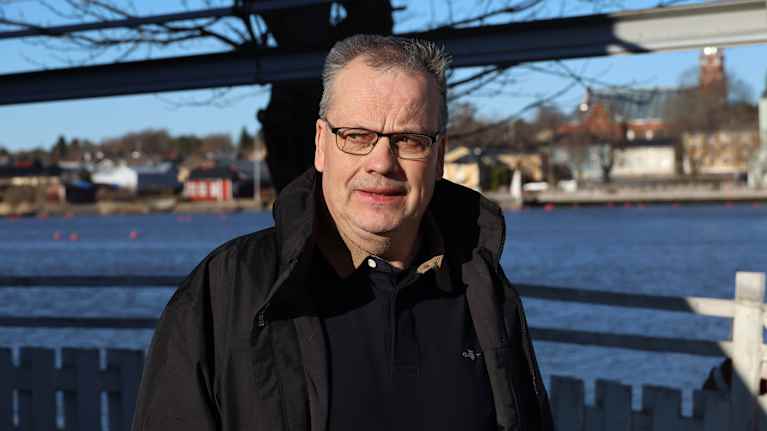 En man med glasögon ser bekymrad ut. I bakgrunden syns havet och byggnader.