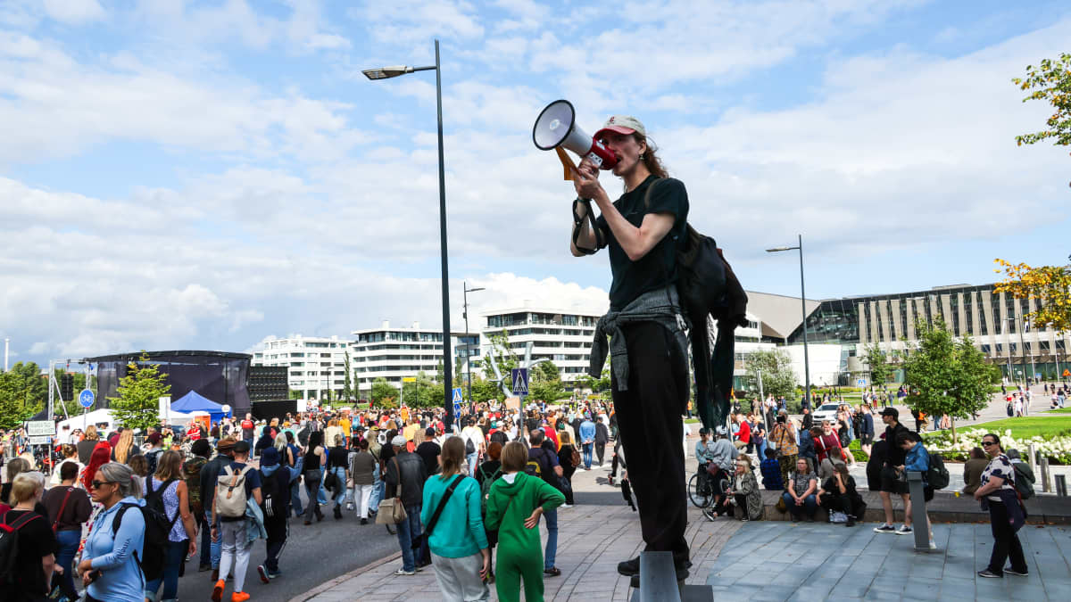 Henkilö megafonin kanssa ohjaa mielenosoittajia oikeaan suuntaan.