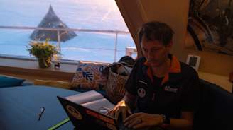 Ihminen työskentelee laivassa, ikkunasta näkyy teltta.