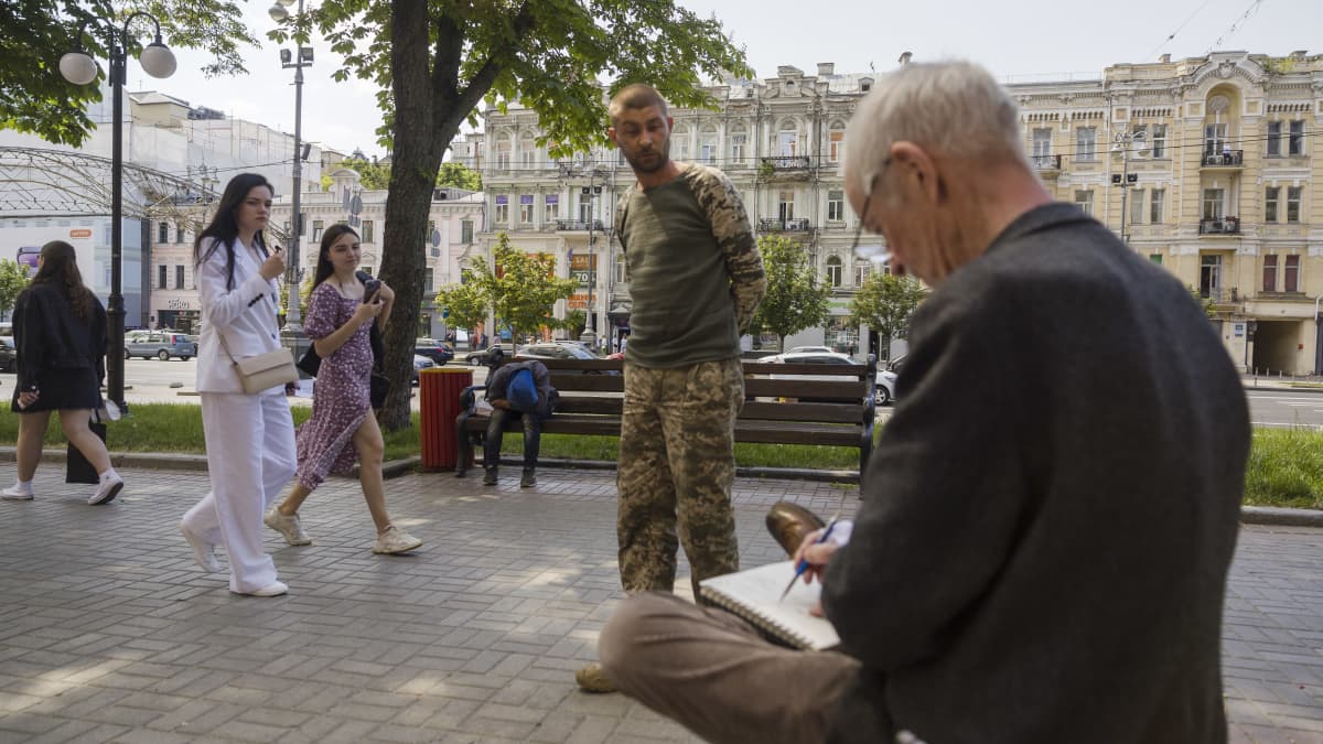 Sarjakuvataiteilija Heikki Paakkanen istuu Kiovan keskustassa ja piirtää, ihmiset kadulla katsovat työtä.