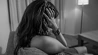 Photo shows a woman sitting on a sofa holding her head in her hands.