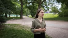 Vihreäpaitainen nainen seisoo puistossa katsoen kameran oikealle samalla puristaen sormiaan yhteen.