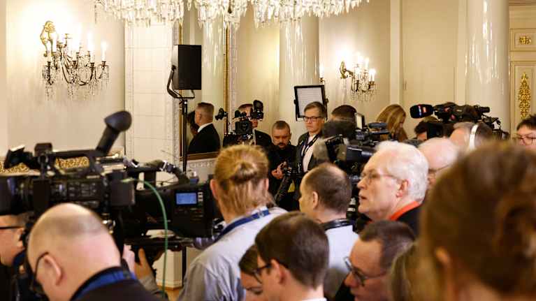 Lehdistöä lehdistötilaisuudessa presidentinlinnassa. Huoneessa valkoisia pylväitä ja kristallikruunuja.
