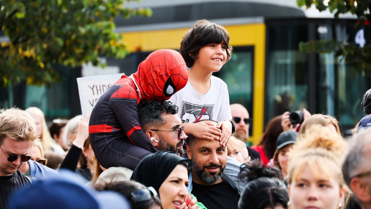 Hämähäkkimies pukuun pukeutunut lapsi isänsä olkapäillä mielenosoittajien keskellä.