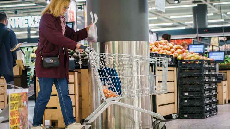 En kvinna lägger en plastpåse med några grönsaker i ner i en shoppingvagn i en mataffär.