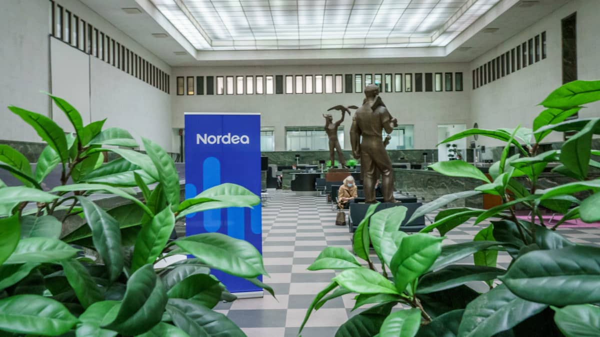 Sisäkuva Nordean suuresta pankkikonttorista. Keskellä banneri jossa lukee Nordea. Etualalla kasveja, taustalla pronssipatsaita ja pari asiakasta.