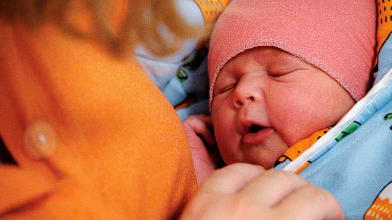 A 24-hour-old baby wrapped in a colorful blanket next to its mother.
