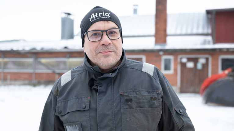 Det verkar som att personen på bilden har på sig en mörk jacka och en mössa med texten "Atrigo". Bakgrunden visar ett snötäckt område med byggnader.