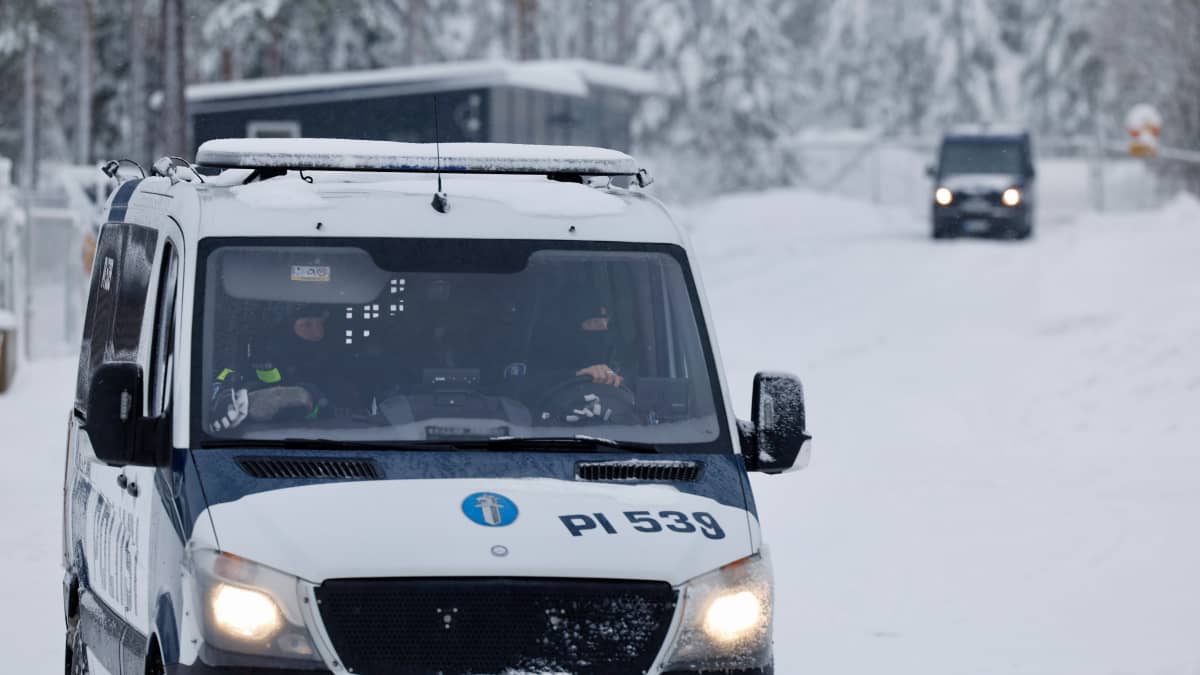 Poliisiautossa kasvot peittävään huppuun pukeutuneita poliiseja lumimaisemassa.