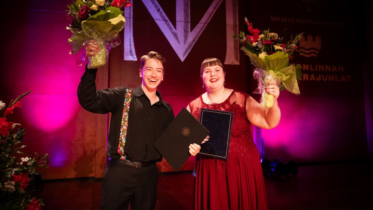 Gabriel Kivivuori Sereno ja Iirisilona Segerstam seisovat vierekkäin ja hymyilevät kameralle. Heillä on molemmilla käsissään kukkakimput ja todistukset.