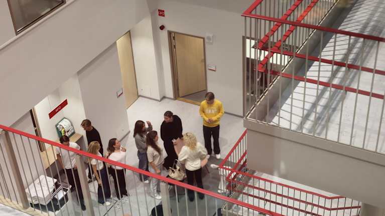 Ett tiotal personer står och samtalar i en korridor vid en trappa inomhus.