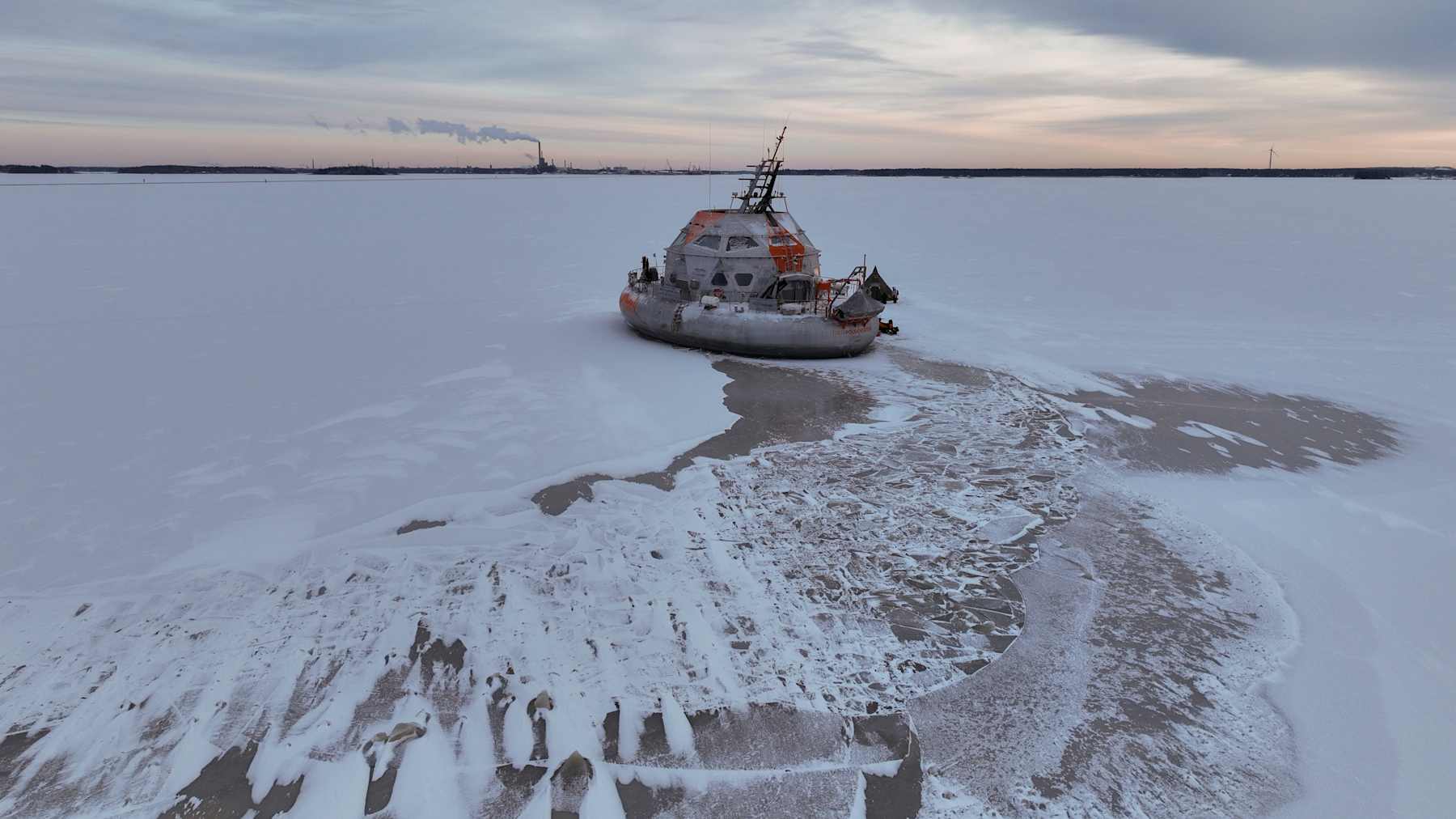 Tutkimusalus on jäässä, horisontissa näkyy tehdas.