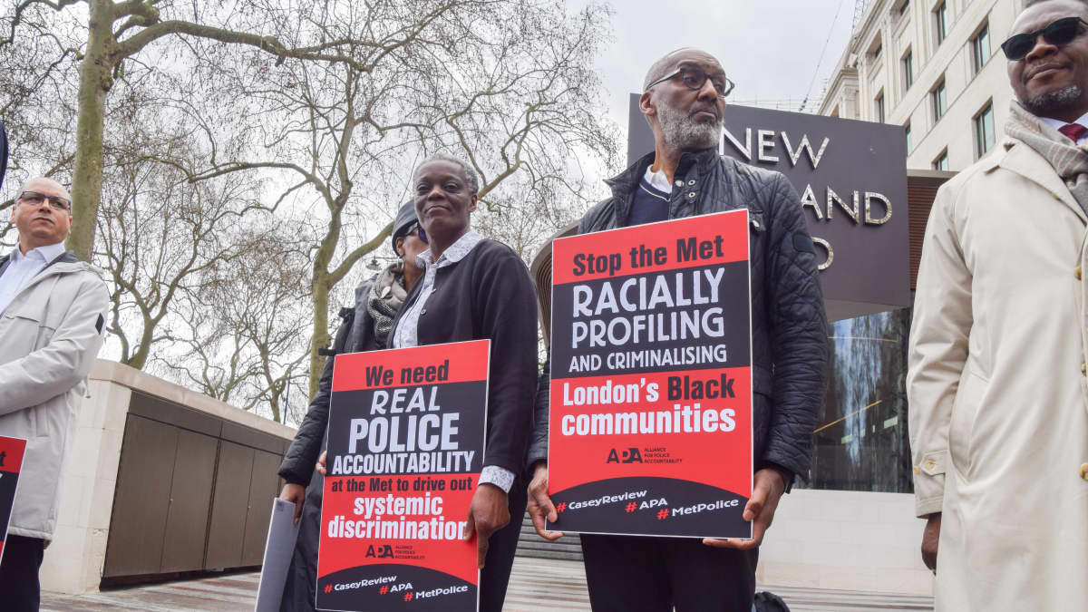 Nainen ja mies pitelevät kylttejä, joissa Lontoon poliisia vaaditaan vastuuseen syrjinnästä ja lopettamaan etnisen profiloinnin.
