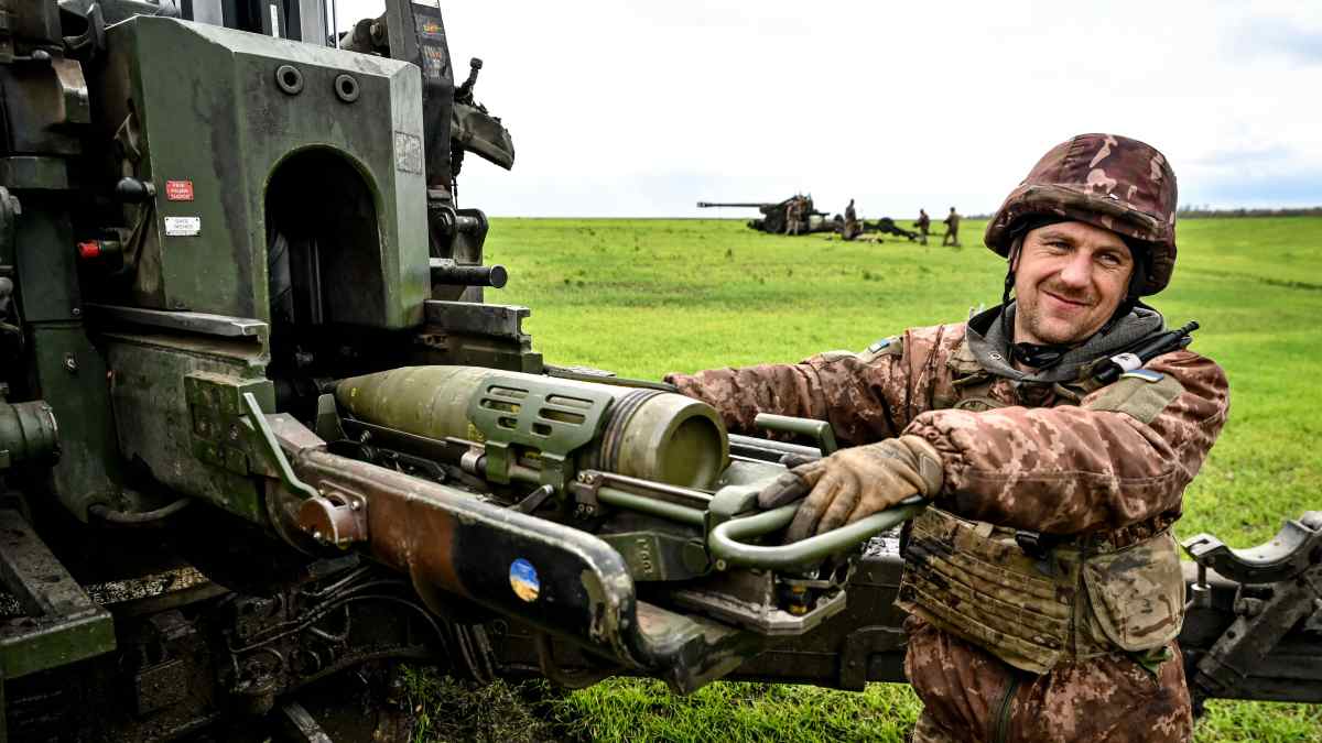 Hymyilevä ukrainalainen sotilas lataa tykkiä. Taustalla toinen tykki. 