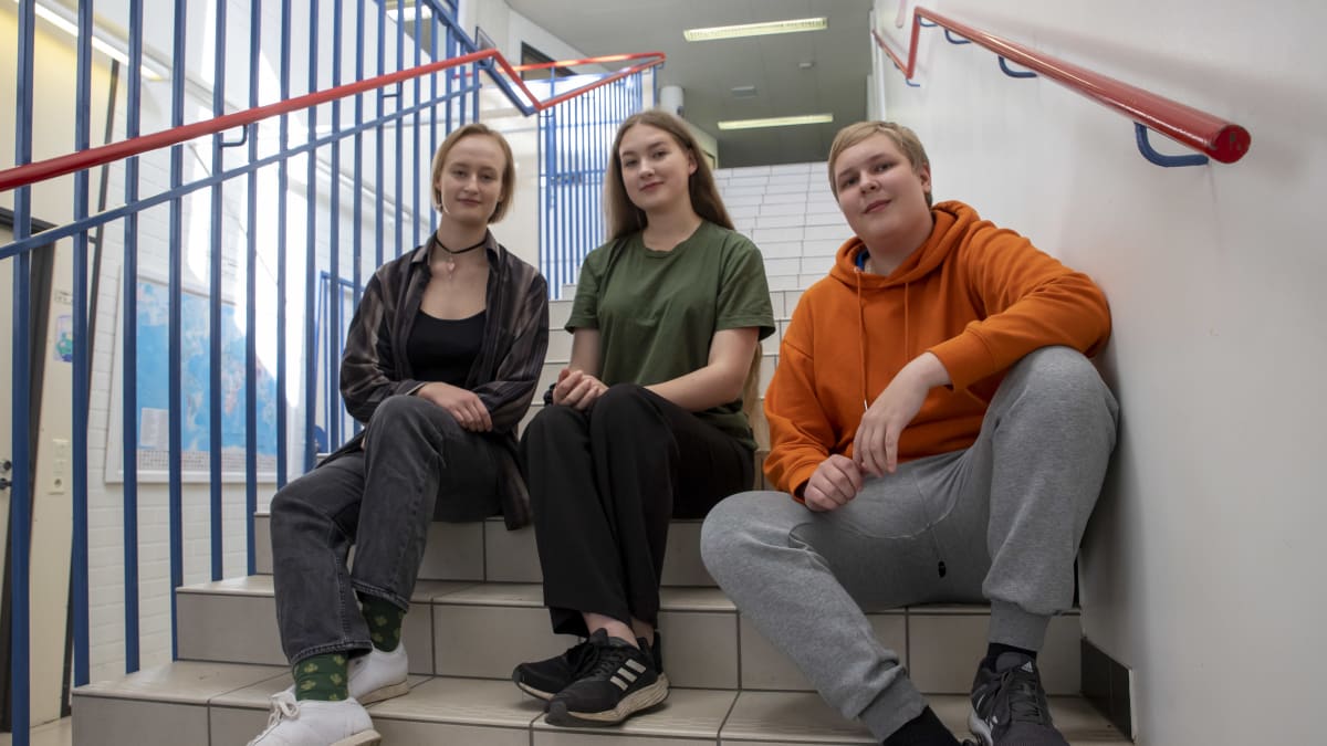Tiia Vallinkoski, Bea Janhonen ja Akseli Vilpponen istuvan Muuramen lukion portailla ja hymyilevät kameralle.