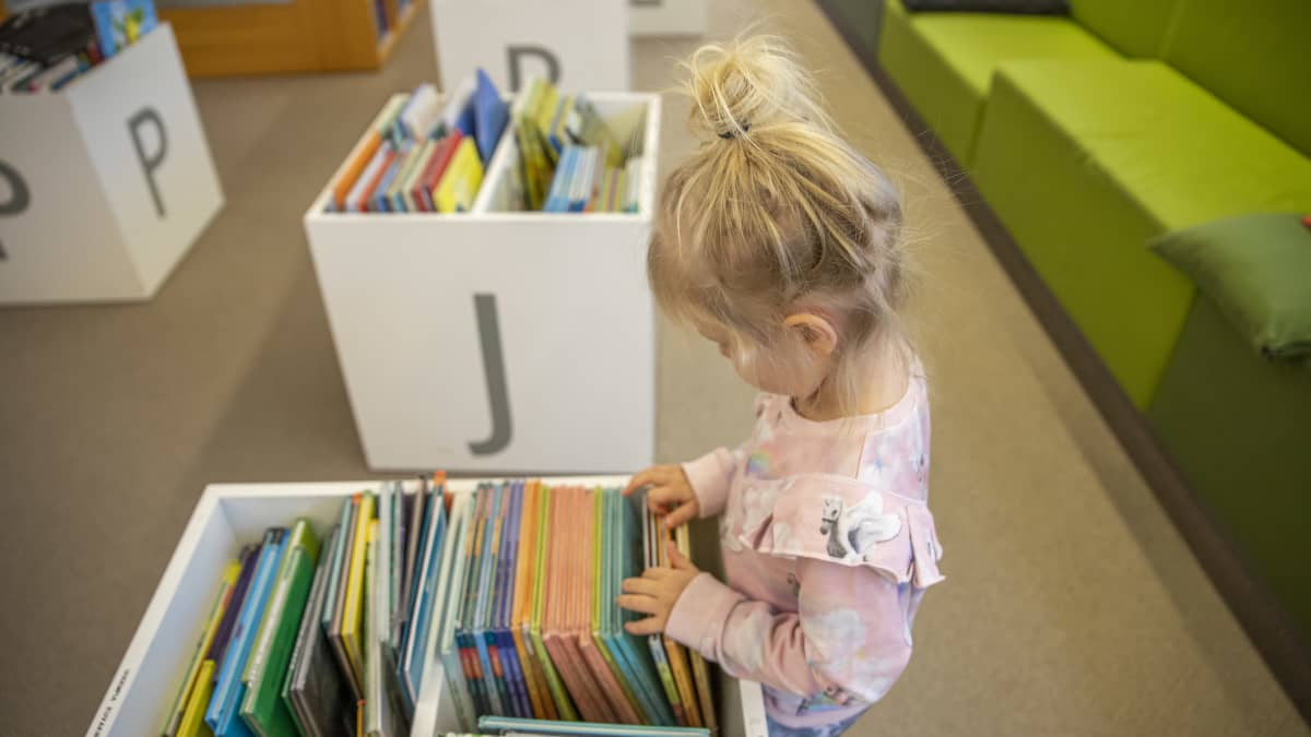 Lapsi tutkii kirjastossa  kirjoja.
