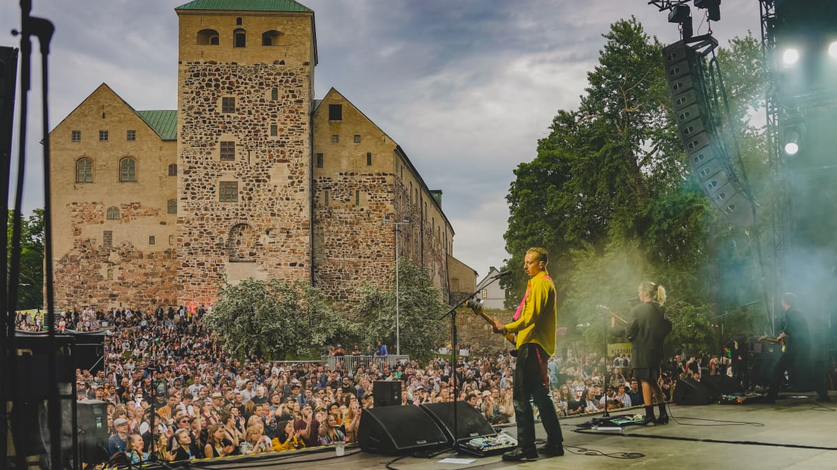 Members of English rock band Wolf Alice play before a large crowd with Turku Castle in the background during the Kesärauha festival in 2022.
